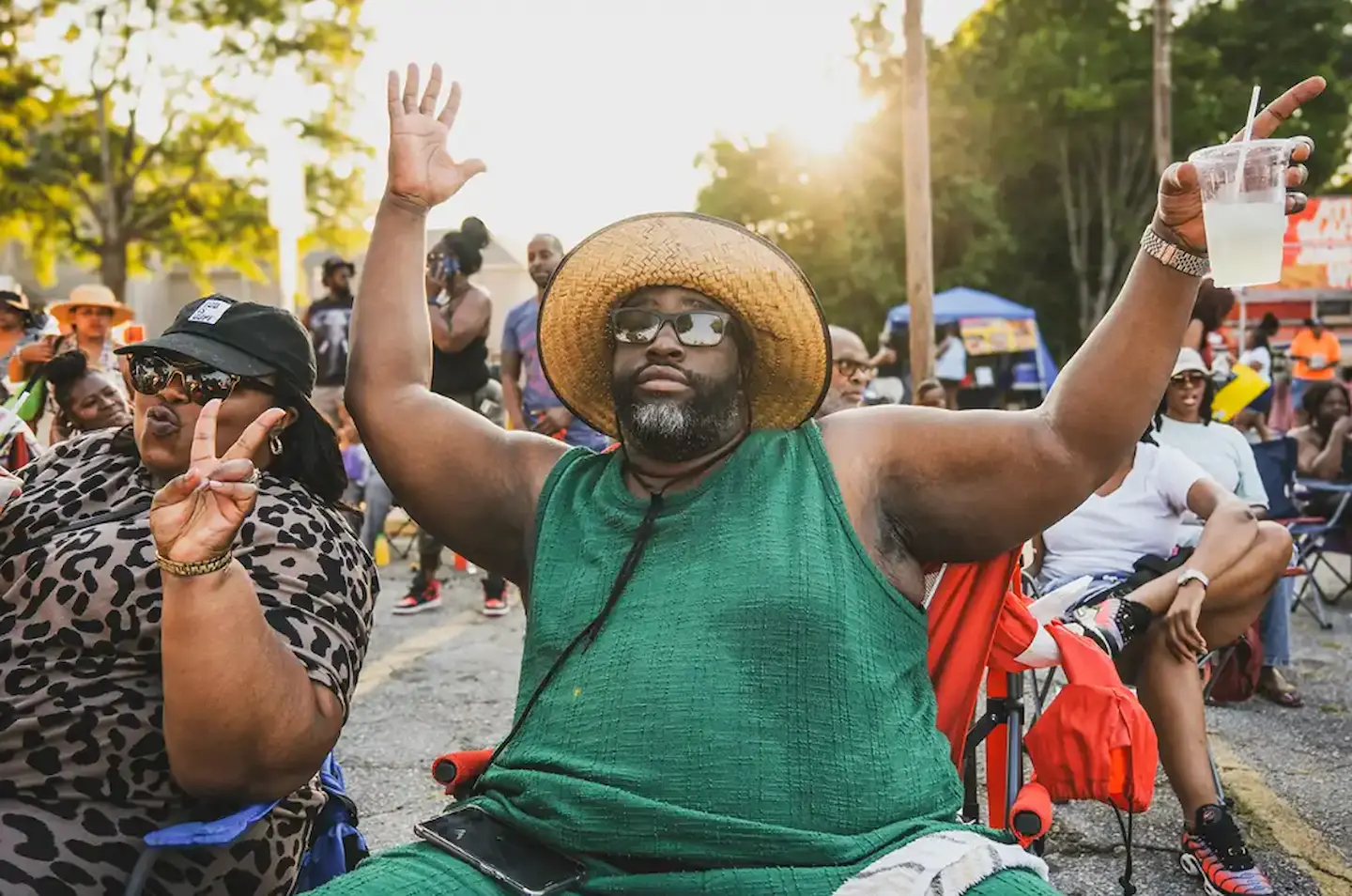 A man with a green shirt and straw hat holding up his hands.